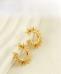 Macro shot of gold fan-shaped sunflower stud earrings resting on white ceramic tray