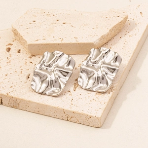 Macro detail of silver stainless steel earrings with irregular crinkled texture on travertine stone