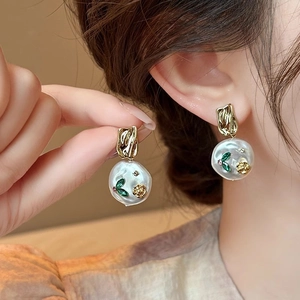 Detail of gold floral earrings with Baroque pearls and green leaves on model