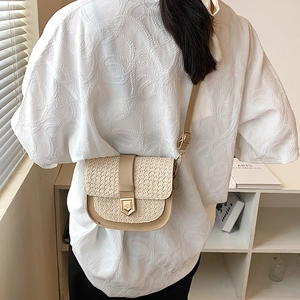 Retro woven straw saddle bag with leather trim and gold buckle shown on shoulder