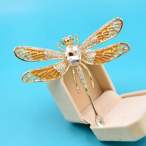 Macro view of golden dragonfly brooch with orange enamel and faceted crystal detail