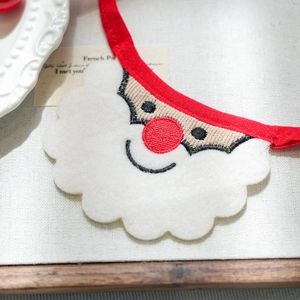 Macro detail of Christmas Santa embroidery on white felt pet bandana with red ribbon ties