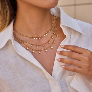 Close-up of triple-layered gold ball chain necklace with sparkling teardrop zircon pendant