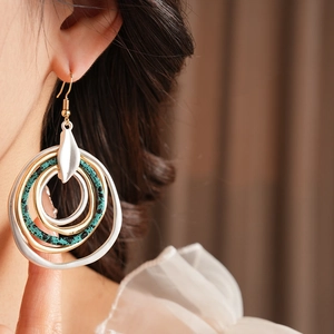 Close-up of layered irregular round metal earrings with turquoise accents on a model