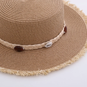 Close-up of woven straw hat featuring seashell decorations and fringe brim detail