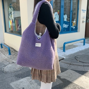 Detail of purple faux shearling tote bag with a woven logo tag and soft fuzzy texture