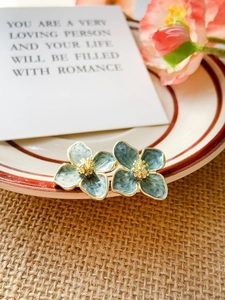 Detail of grey-blue enamel flower earrings on a ceramic dish with rustic decor