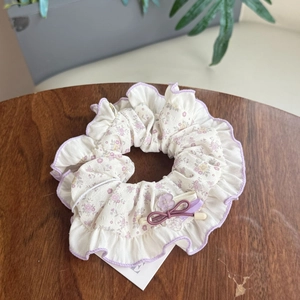 Detail eines floralen Haargummis mit lila Spitzenkante, Schleife und Herzanhänger