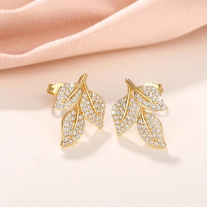 Detailed view of gold leaf stud earrings with sparkling pavé crystals on pink silk fabric