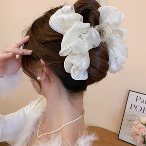 Detail of cream organza bow hair claw clip with rhinestones worn by a model in a bun
