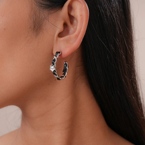 Détail d'une boucle d'oreille créole tressée en chaîne argentée et cuir noir sur modèle