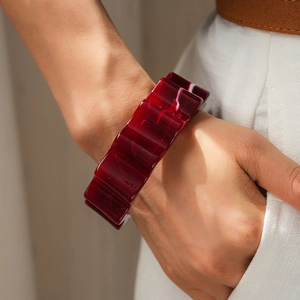 Dettaglio di un bracciale in acrilico bordeaux a forma di ingranaggio sul polso di donna
