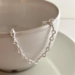 S925 sterling silver chain bracelet with twisted heart links on a white ceramic cup