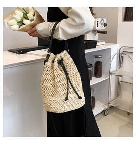 Beige woven straw bucket bag detail with black drawstring and golden hardware accents