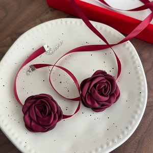 Elegant deep red fabric rose choker necklaces with silk ribbons on a decorative white plate