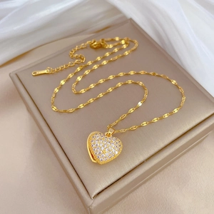 Elegante goldene Titankette mit glitzerndem Herzanhänger auf einer Champagner-Schmuckschachtel