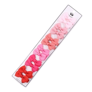 Set of 12 grosgrain ribbon bow hair clips in pink to red gradient colors on a white card