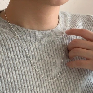 Detail of a minimalist 925 sterling silver bead necklace worn on a grey knit sweater