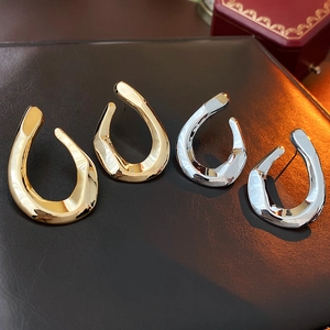 Close-up of sleek gold and silver twisted U-shaped earrings on leather surface