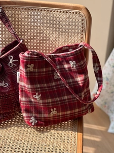 Détail du sac cabas à carreaux rouges avec broderie nœud blanc et étiquette latérale