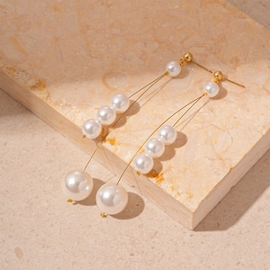 Detail of vintage gold pearl tassel earrings with geometric fringe on a stone surface
