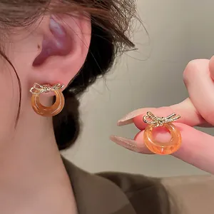 Elegant gold bow earrings with amber resin hoop shown on a model for scale and style