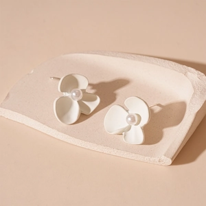 Macro detail of white matte flower earrings with center pearl on minimalist stone tray