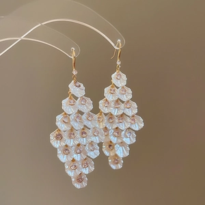 Detailed macro view of cascading gold fringe earrings with white shell petals and pink crystals