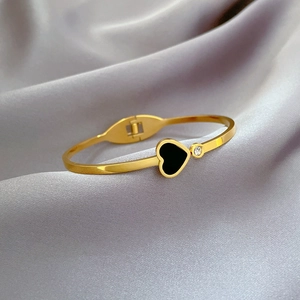 Detail of gold titanium heart bangle with black inlay and zircon on silk background