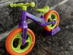 Close-up of purple balancing car toy with orange wheels on a textured stone surface