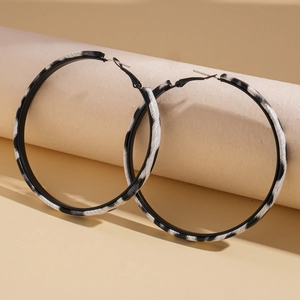 Detailed close-up of large black and white zebra pattern hoop earrings on beige background