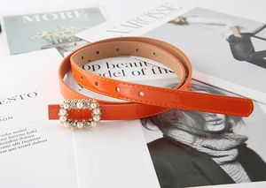 Detail of orange slim leather belt with a square pearl and rhinestone buckle