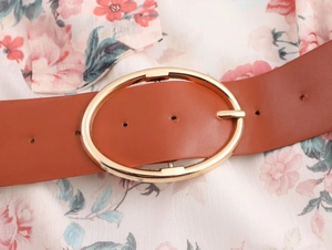 Close-up of brown leather belt with gold oval buckle on a floral chiffon midi dress