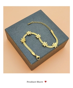 Macro shot of gold daisy blade chain bracelet with five flower charms on a gray box