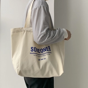 Side view of large cream canvas tote bag with blue lettering on a female shoulder