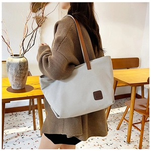 Off-white canvas tote bag with brown leather straps styled in a modern indoor lifestyle scene