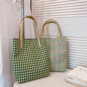 Détails de sacs fourre-tout à carreaux verts avec anses en cuir sur fond minimaliste