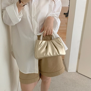 Detail of golden ruched cloud bag featuring elegant pearl handle and soft leather texture