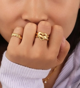 Close-up of golden S925 sterling silver heart knot and paved rings on model's finger