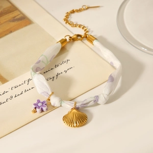 Detail of silk scarf bracelet with purple floral print and golden seashell charms