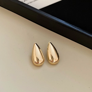 Detailed close-up of golden teardrop earrings with a smooth polished metallic finish