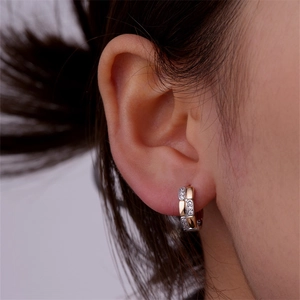 Macro shot of two-tone twisted huggie earrings with silver pavé zircons and gold mirror finish