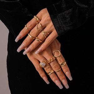 Detail of stacked gold geometric rings including chain, twist, and pearl styles on model's hand