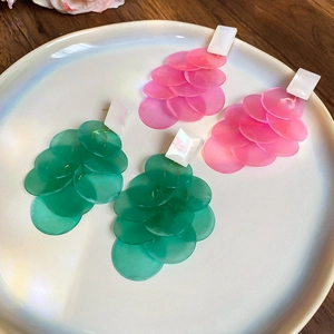 Detailed view of layered fuchsia and green shell tassel earrings on a ceramic dish