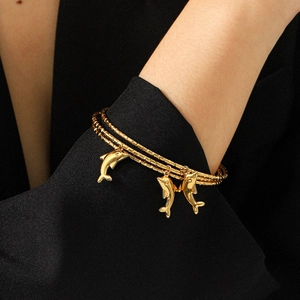 Dreilagiges 18k Gold Delphin-Anhänger Armband am Handgelenk auf schwarzem Hintergrund