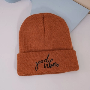 Detail of caramel orange knit beanie featuring black 'good vibes' script embroidery