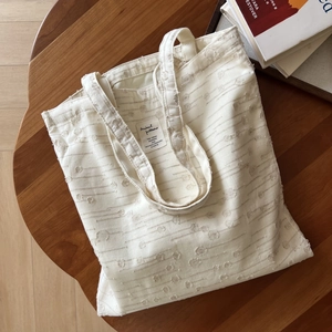 Detail view of white textured cotton tote bag with minimalist label on a wooden table