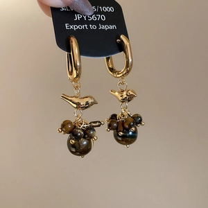 Macro detail of 18k gold bird stud earring with tiger eye stone beaded tassels
