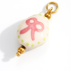 Macro shot of an oval cream enamel unicorn charm with a pink bow and gold loop
