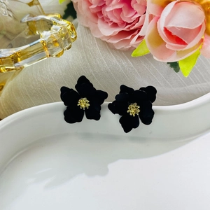 Close-up of black flower earrings with gold center on a white wavy display tray